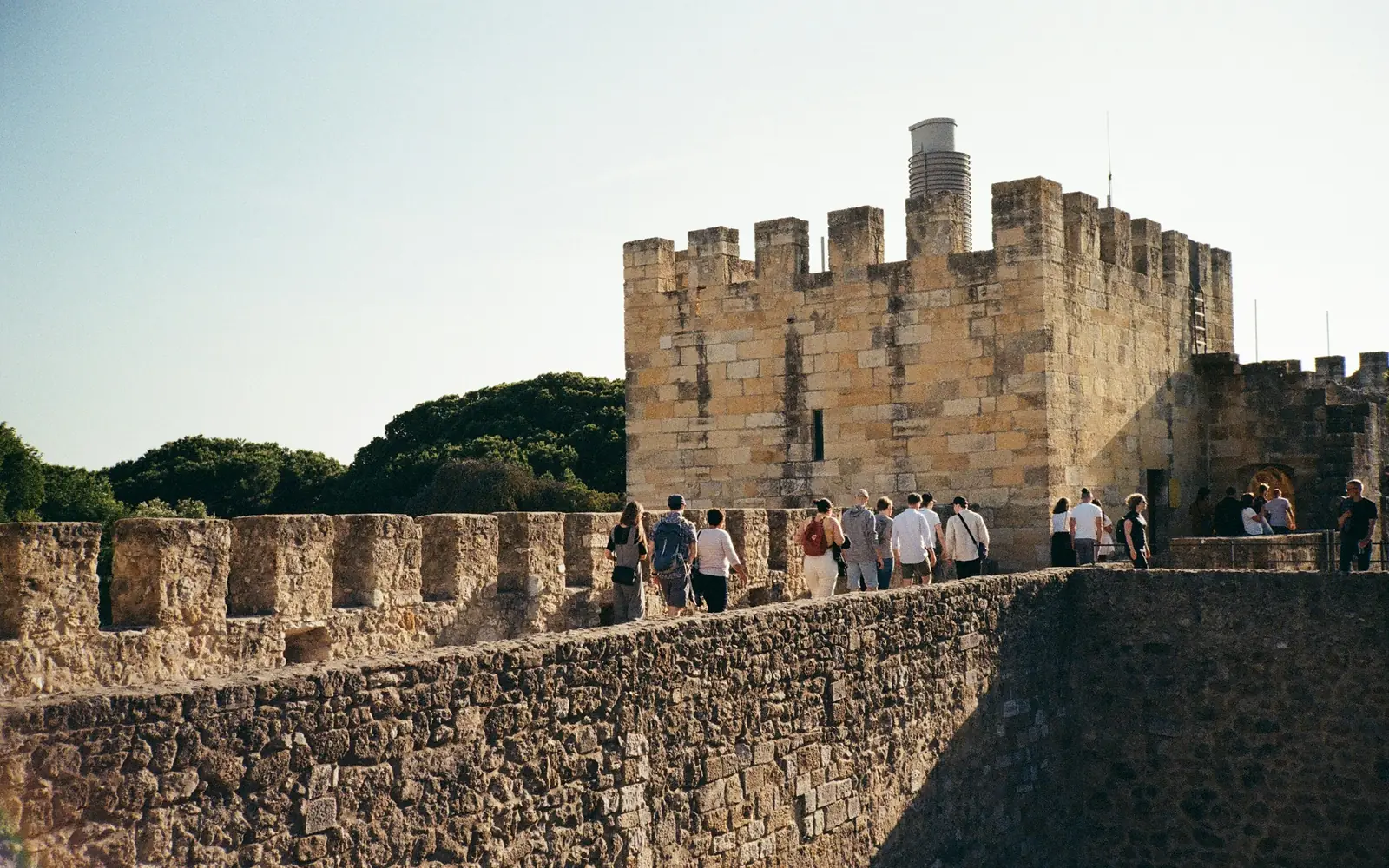 A square stone tower of Castelo de São Jorge with visitors below